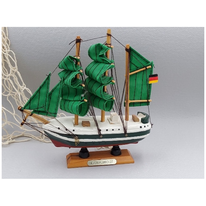 Auf einem Holzständer mit der Aufschrift „Alexander von Humboldt ca.16cm Holz“ steht ein detailreiches Modell eines Segelschiffs. Das Schiff hat grüne Segel, eine deutsche Flagge am Heck und eine aufwendige Takelage. Im Hintergrund ist teilweise ein Fischernetz zu erkennen.