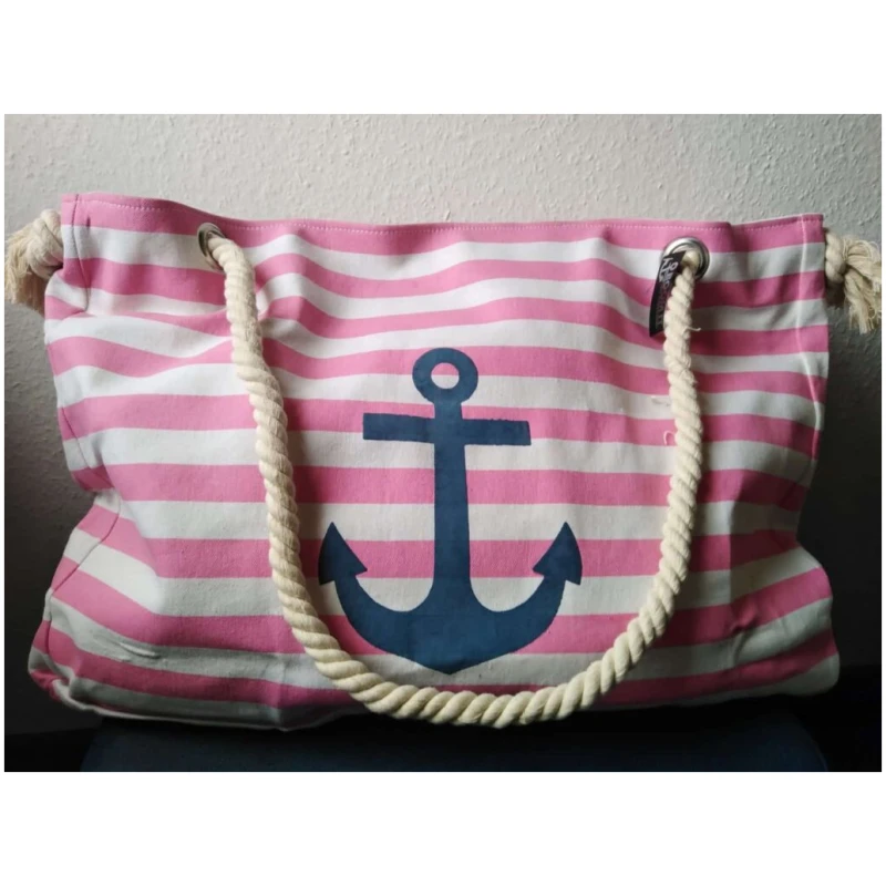 Ein rosa-weiß gestreifter Stockschirm „Maritim“ Anker Streifen Regenschirm mit einem großen blauen Ankermotiv, das dem Anker-Logo auf der Vorderseite ähnelt. Die Tasche hat dicke, gedrehte Seilgriffe, die an silbernen Ösen befestigt sind. Der Hintergrund ist eine helle Wand.