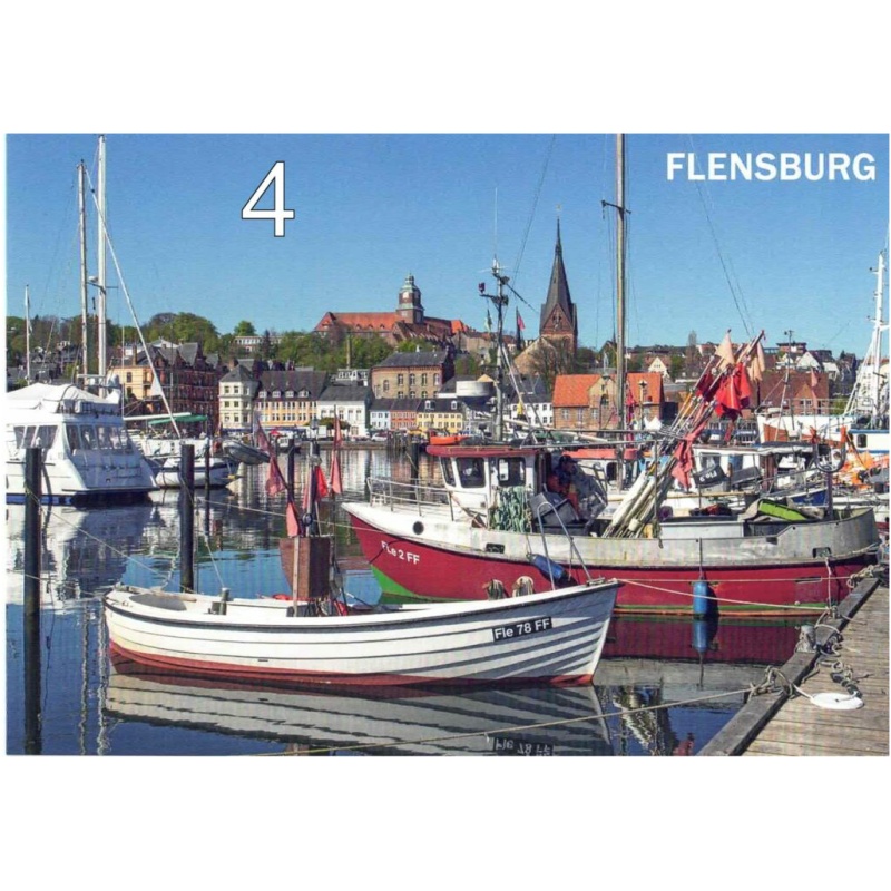 Eine malerische Aussicht auf einen Jachthafen in Flensburg, Deutschland, erinnert an eine malerische Postkarte mit Motiven aus Flensburg und Umgebung. Mehrere Boote liegen dort, darunter ein kleines weißes Boot und rote Fischerboote. Im Hintergrund ist die Stadt mit ihren farbenfrohen Gebäuden und Kirchen mit markanten Kirchtürmen unter einem klaren blauen Himmel zu sehen.