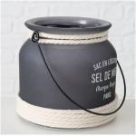 Exklusives Highline Windlicht Seldemer, Beige, Grau, Weiss Ein grauer Metallbehälter mit schwarzem Griff und weißem Seil, das oben und unten umwickelt ist. Er trägt den französischen Text „SAC EN LOCATION SEL DE MER Marque Rouge PARIS“. Dieser Highline Dekoaufsteller Saily steht vor einem weißen Ziegelhintergrund.