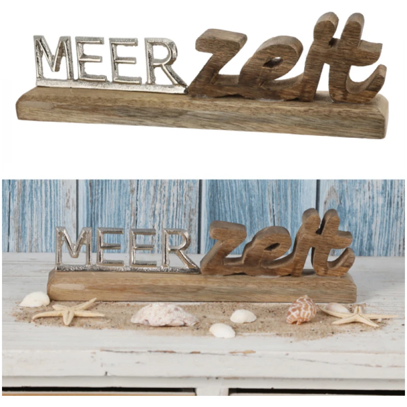 Ein Schriftzug Meerzeit, Silber mit der Aufschrift „Meerzeit“ in silbernen und braunen Buchstaben steht elegant auf einem Holzsockel. Der Hintergrund besteht aus hellblauen, verwitterten Holzpaneelen, während Muscheln und Seesterne kunstvoll auf einer weißen, sandbestreuten Oberfläche verstreut sind.