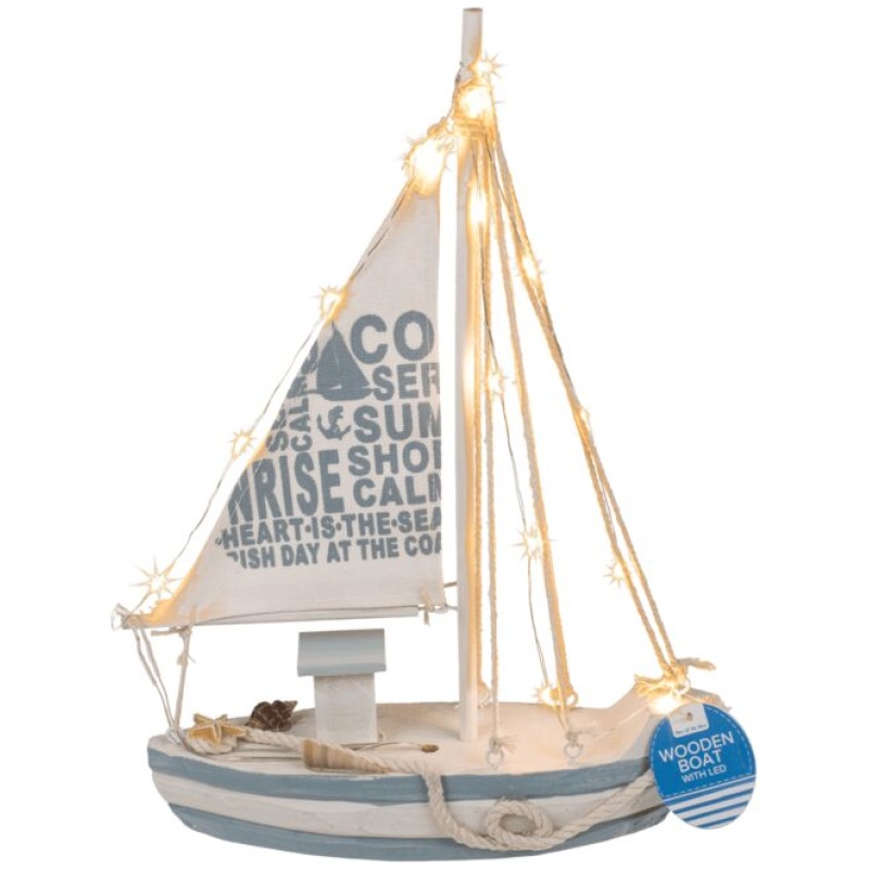 Ein kleines dekoratives Segelboot aus Holz mit Lichterketten um den Mast und einer Glitterkugel, Maritim, auf Sockel mit tollen Motiven an der Basis. Das Segel trägt die Aufschriften „COAST“, „SERENE“ und „SHORE“. Das Boot ist blau-weiß lackiert und an der Vorderseite hängt ein Schild mit der Aufschrift „WOODEN BOAT DECO“.