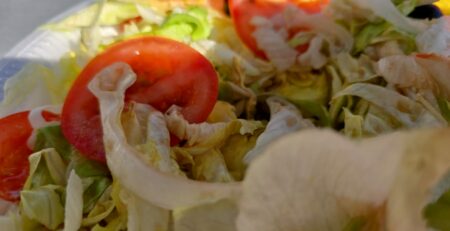 Nahaufnahme eines gemischten Salats mit geschnittenen Tomaten, Eisbergsalat und möglicherweise anderem Gemüse. Die Farben sind lebendig und heben die Frische der Zutaten hervor. Das Bild scheint bei natürlichem Licht aufgenommen worden zu sein, wodurch die Textur des Salats und der Tomaten hervorgehoben wird.