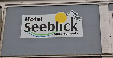 Schild des Hotels Seeblick Appartements mit Logo und Sonne, das die Unterkunft anzeigt, ideal für Reisende und Touristen.