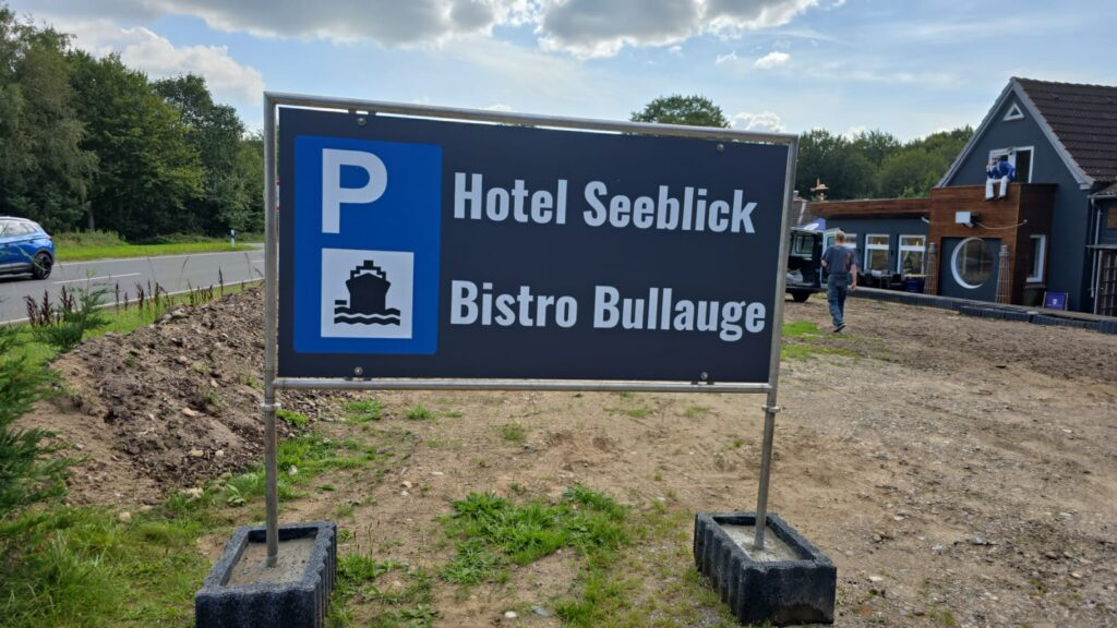 Schild mit Parkplatzinformation für Hotel Seeblick und Bistro Bullauge, zeigt Logo und Namen, umgeben von Natur.