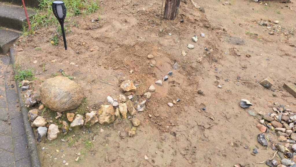 Gartenbereich mit Steinen, Erde und einem Holzpfosten, ideal für Landschaftsgestaltung oder Gartenprojekte.