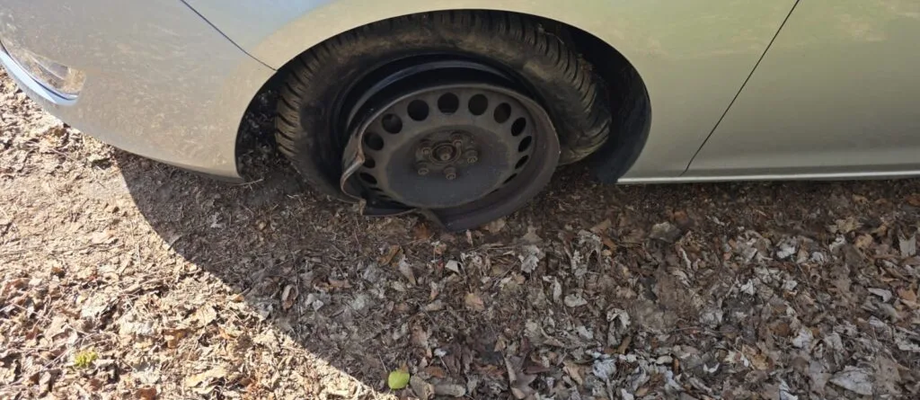 Ein silbernes Auto mit einem plattgefahrenen Reifen auf einem unebenen Boden.