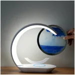 3D Sanduhr - Sandmalerei - Nachttischlampe mit drahtloser Handyladestation Moderne Tischlampe mit einem Hand, die ein rundes Wasserfarbengemälde hält.