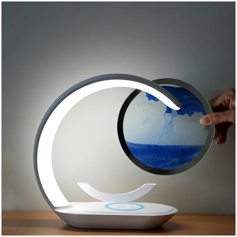 3D Sanduhr - Sandmalerei - Nachttischlampe mit drahtloser Handyladestation Moderne Tischlampe mit einem Hand, die ein rundes Wasserfarbengemälde hält.