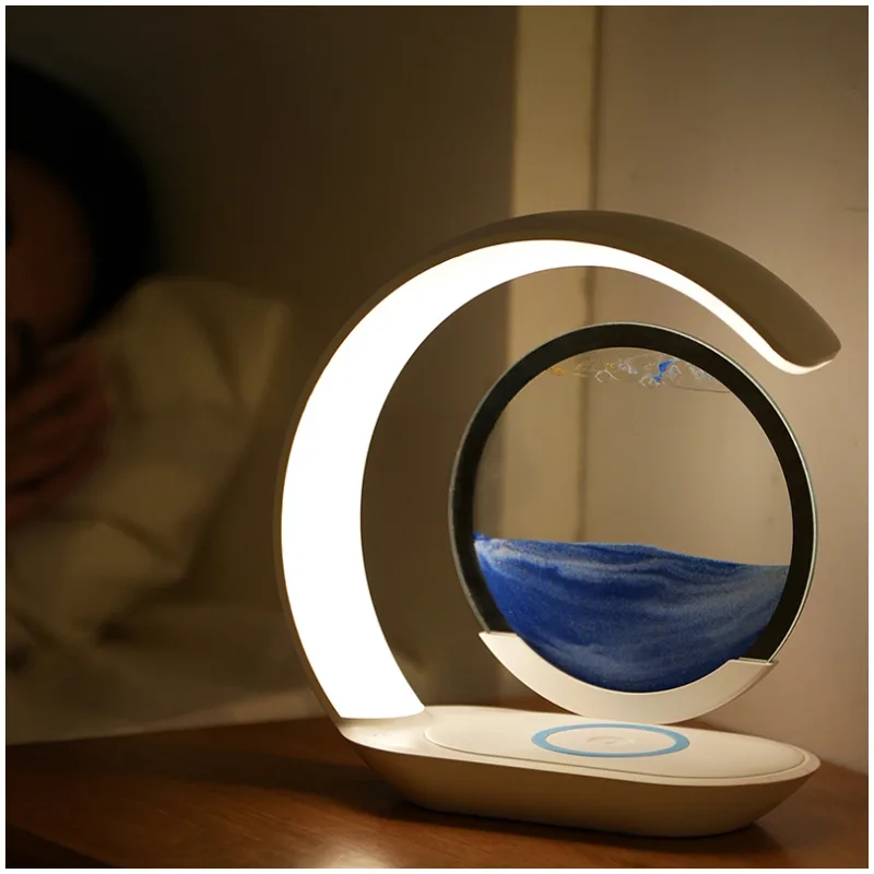 3D Sanduhr - Sandmalerei - Nachttischlampe mit drahtloser Handyladestation Moderne Tischlampe mit einem runden Sanduhr-Element und LED-Beleuchtung auf einem Nachttisch.