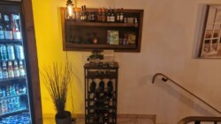 Ein Weinregal mit verschiedenen Weinen und Gläsern, daneben eine Kühlvitrine mit Getränken in einem gemütlichen Raum.